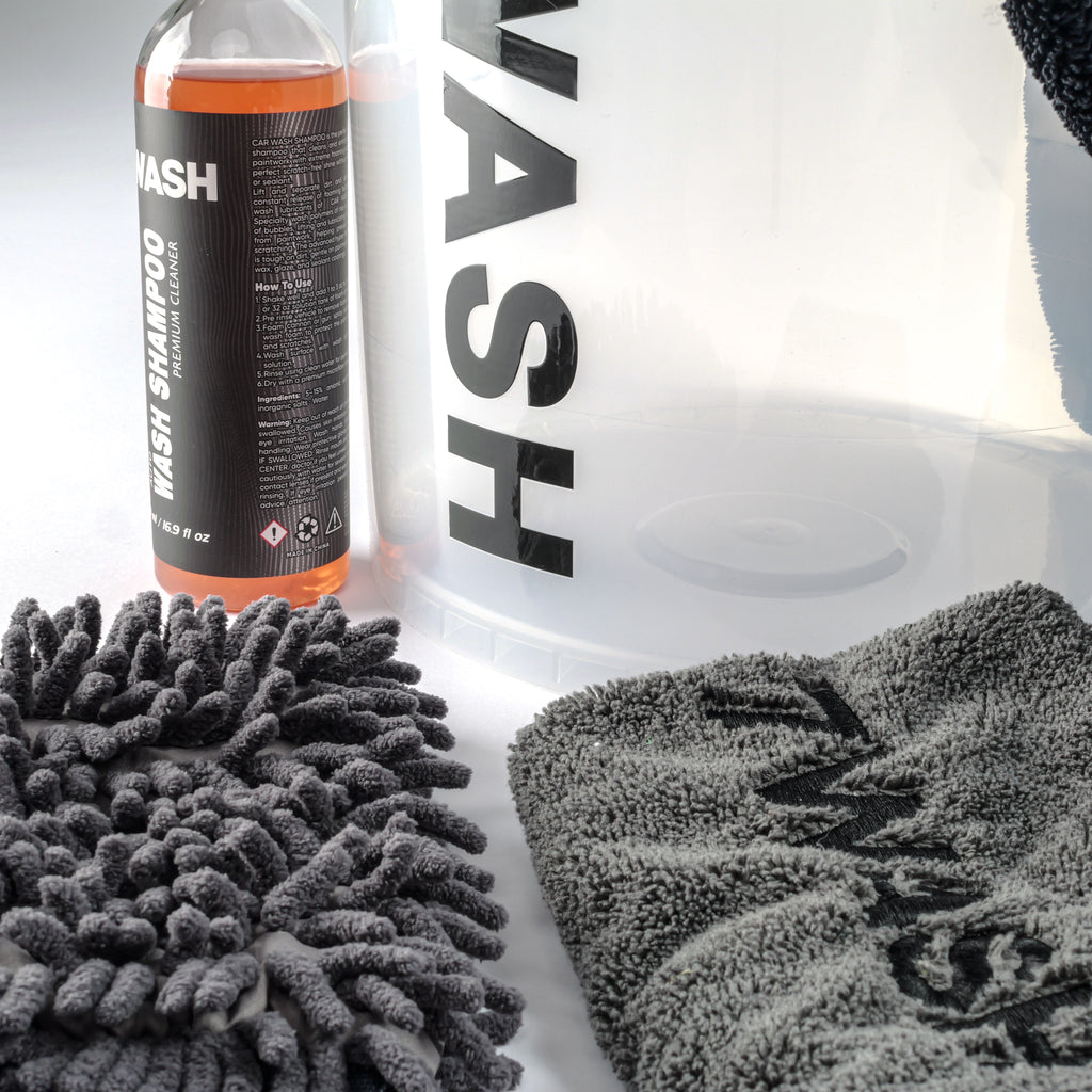 7WASH Starter Wash Set bestehend aus einem transparenten Wascheimer mit schwarzem Logo, einer 500ml Flasche Autoshampoo, einem grauen Mikrofaser-Waschhandschuh, einem grauen Trockentuch und einem schwarzen Mikrofasertuch.