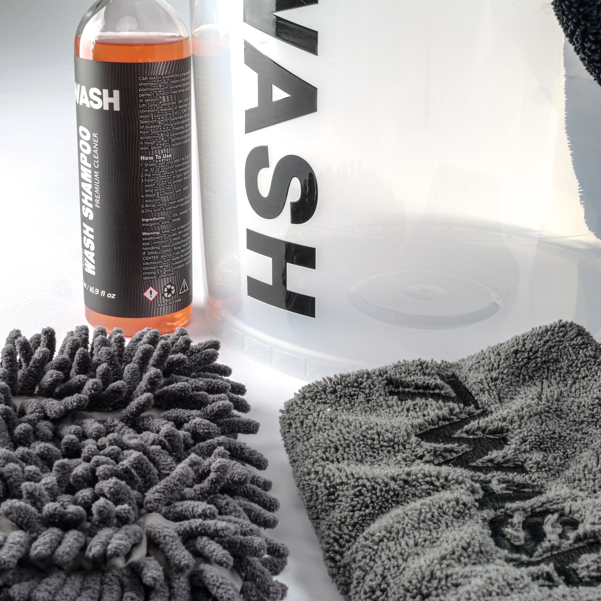 7WASH Starter Wash Set bestehend aus einem transparenten Wascheimer mit schwarzem Logo, einer 500ml Flasche Autoshampoo, einem grauen Mikrofaser-Waschhandschuh, einem grauen Trockentuch und einem schwarzen Mikrofasertuch.